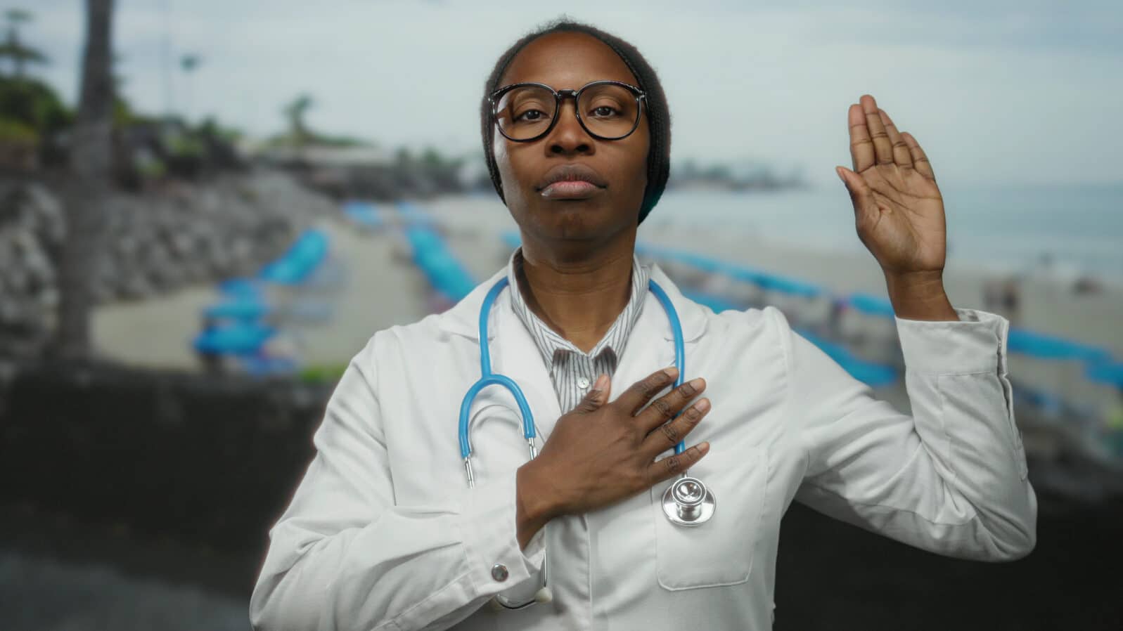 Woman doctor with stethoscope takes an oath at the beach, symbolizing medical commitment in serene seascape.