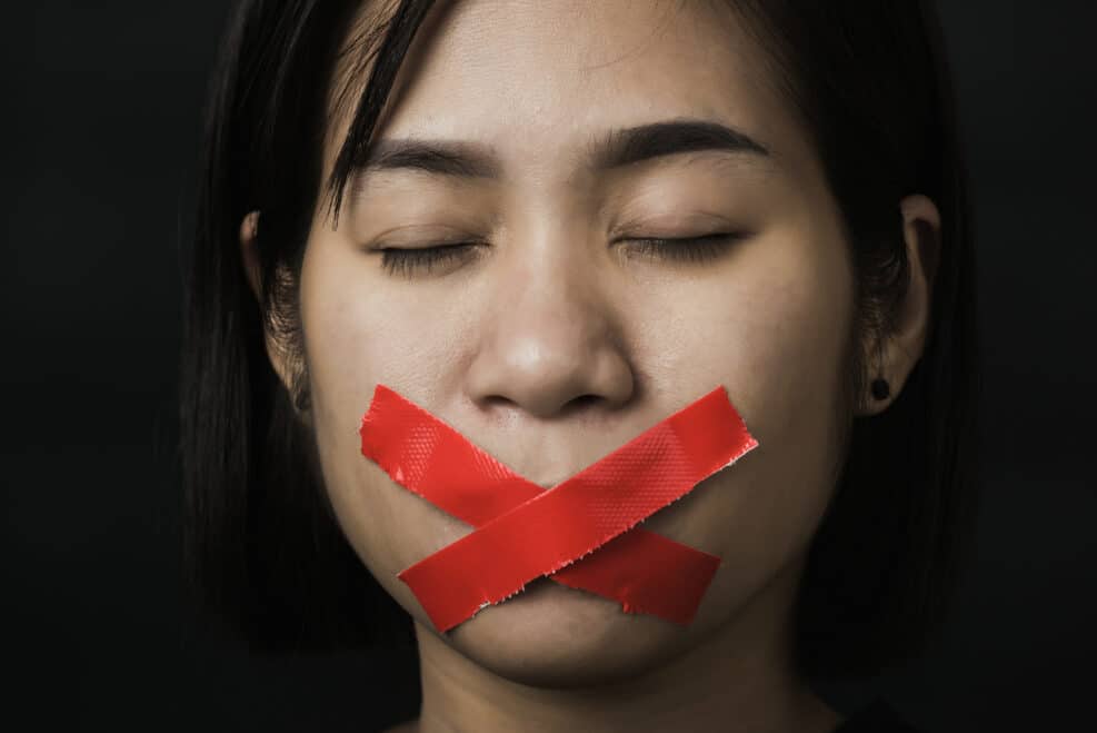 Asian woman blindfold wrapping mouth with red adhesive tape on black background. Freedom speech censorship and stop talk, International Human Right day