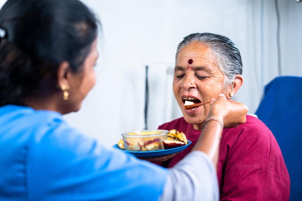 Nurse helping sick senior women to eat fruits at hospital - concept of healthcare, medicare and caretaker
