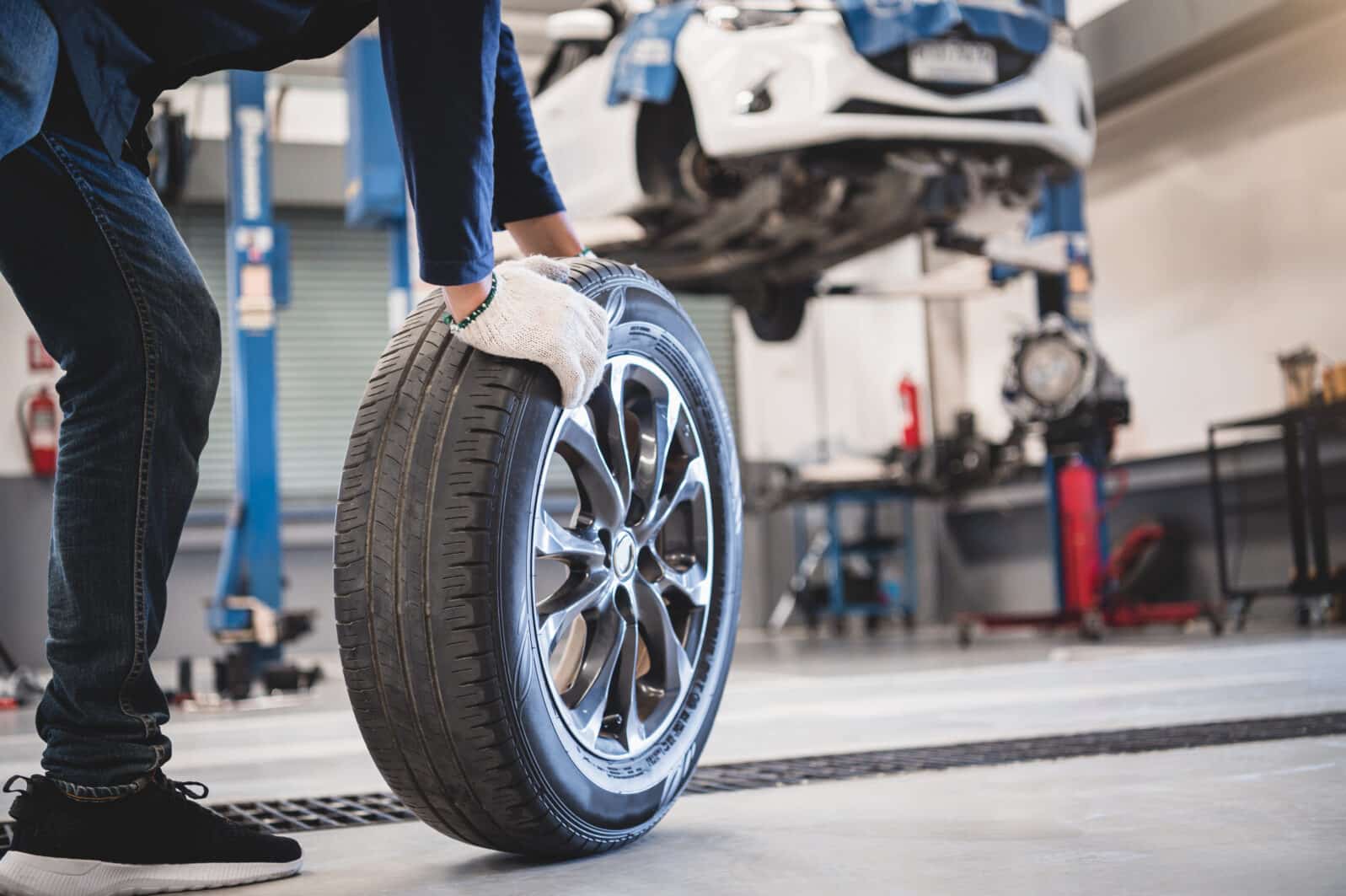 Male mechanic hold and rolling tire at repairing service garage background. Technician man replacing winter and summer tyre for safety road trip. Transportation and automotive maintenance concept