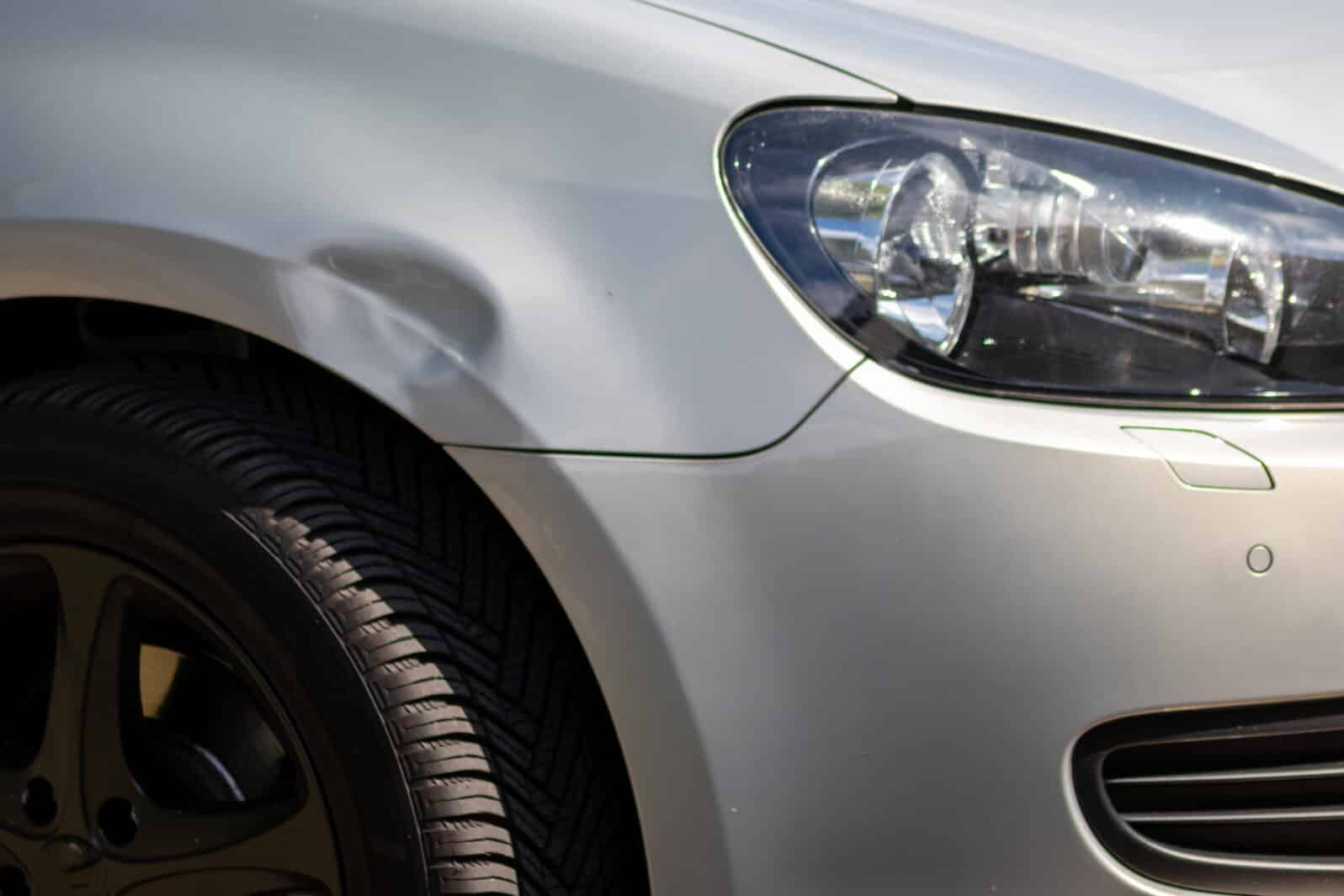 Dented car wing and fender with scratches and bumps after crash and car accident with hit-and-run driving and absconding shows need for car insurance and safety protection and mechanics garage service