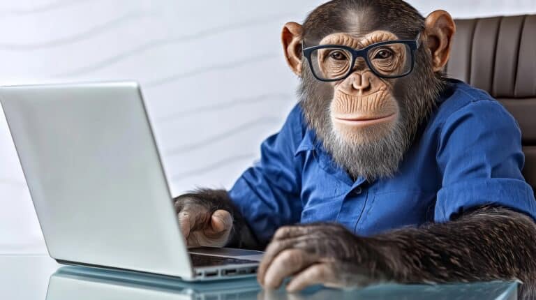 Monkey wearing glasses is sitting at a desk with a laptop. The monkey appears to be working on the laptop, possibly typing or browsing the internet. Concept of humor and playfulness