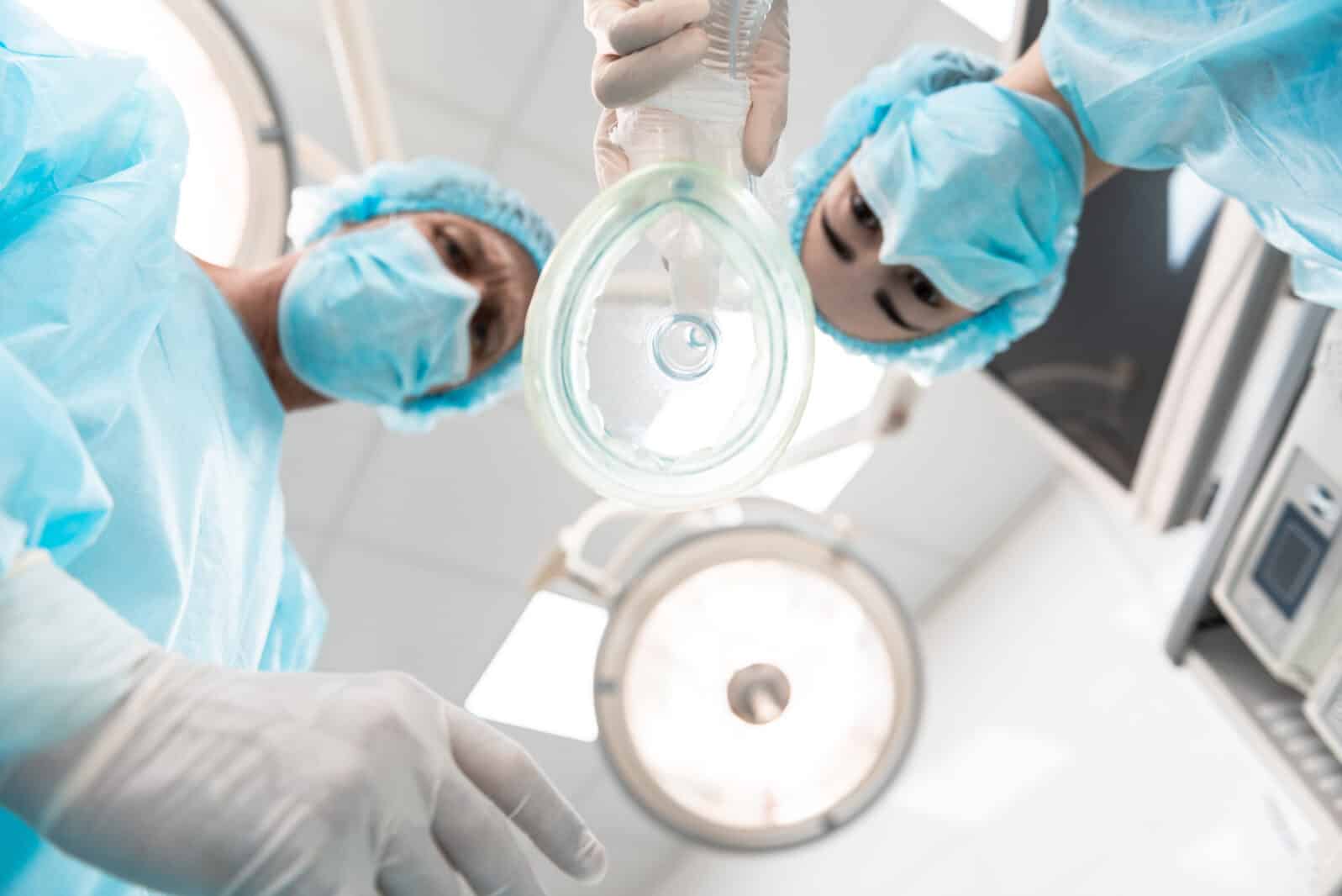 Two serious doctors wearing blue masks and looking at you while standing with the anesthetic mask