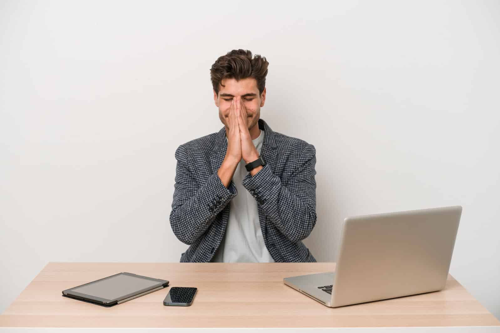 Young entrepreneur man working with a laptop isolated holding hands in pray near mouth, feels confident.