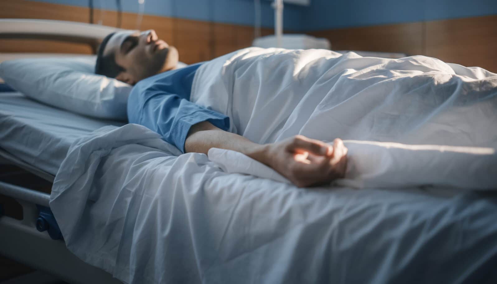 Person lying unconscious or sleeping on a hospital bed with IV drip.